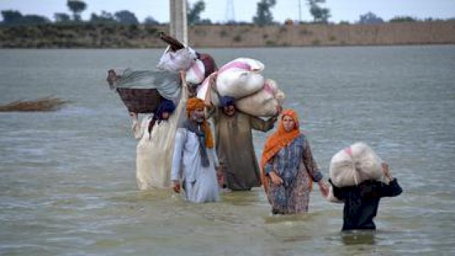 Sebuah keluarga pengungsi mengarungi daerah banjir setelah hujan deras, di Jaffarabad, sebuah distrik di provinsi Baluchistan barat daya Pakistan, Rabu (24/8/2022). foto: AP Photo/Zahid Hussain