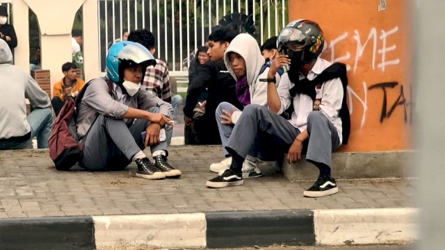 Beberapa anak sekolah duduk di trotoar jalan menunggu aksi demonstrasi selesai. Foto: ist