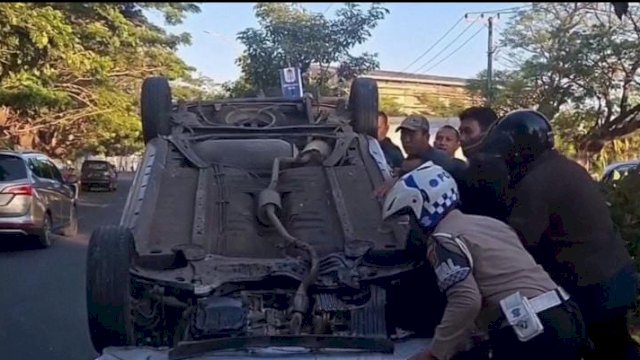 Personel Satlantas Polrestabes Makassar bersama warga berusaha mengevakuasi mobil dari badan jalan.