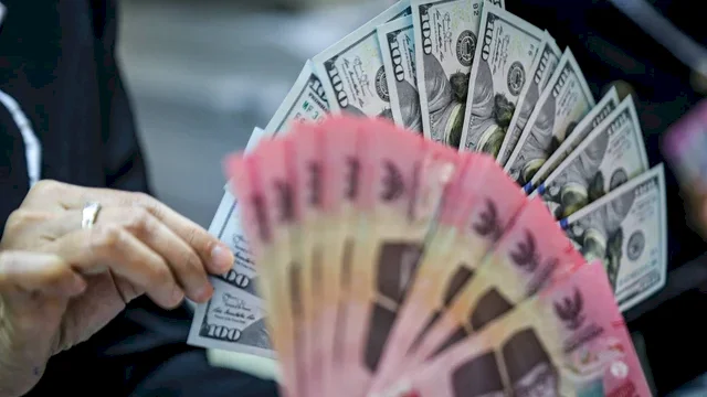 Seorang petugas menunjukan pecahan Dolar AS dan Rupiah di salah satu tempat penukaran mata uang asing di Kwitang, Jakarta, Senin (9/12/2024). Foto: Iqbal Firdaus/kumparan
