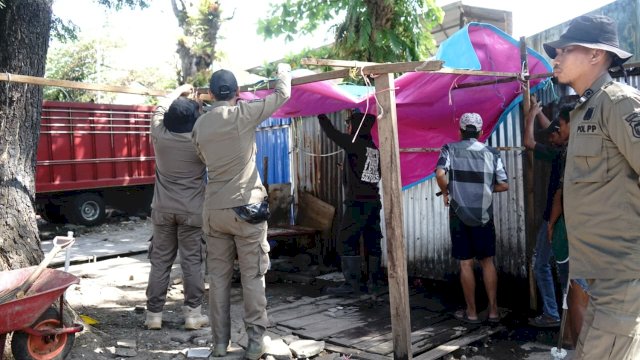 Personel Satpol PP saat bersinergi bersama warga melakukan pembersihan material sisa bangunan semipermanen yang berdiri di atas fasilitas publik di kawasan Kelurahan Ujung Pandang Baru, Kecamatan Tallo.