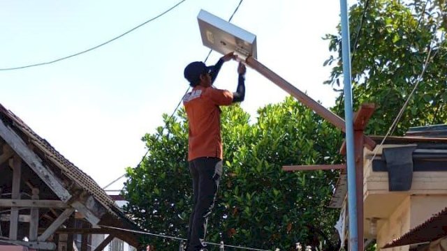 Personel UPT-PJU Dinas Perhubungan Kota Makassar saat menggunakan tangga portabel untuk melakukan instalasi perangkat lampu jalan berbasis tenaga surya di kawasan pemukiman warga kepulauan.