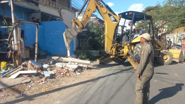 Alat berat dari Dinas PU Makassar diturunkan untuk membantu membongkar sisa material bangunan permanen yang berdiri di atas saluran drainase di Kelurahan Lette, Mariso.